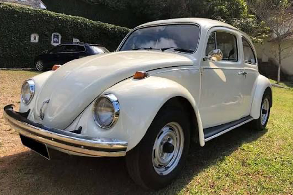Volkswagen Sedán blanco estacionado sobre pasto.